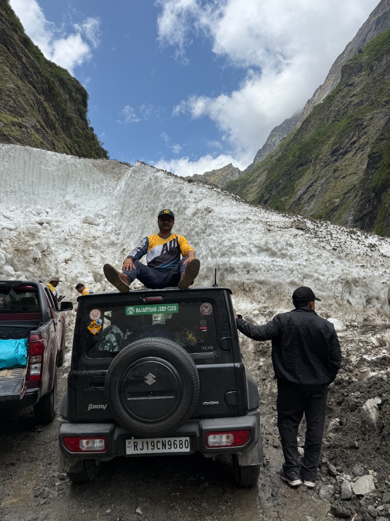 Suzuki Jimny parked in front of a massive wall of snow on the high mountain pass
