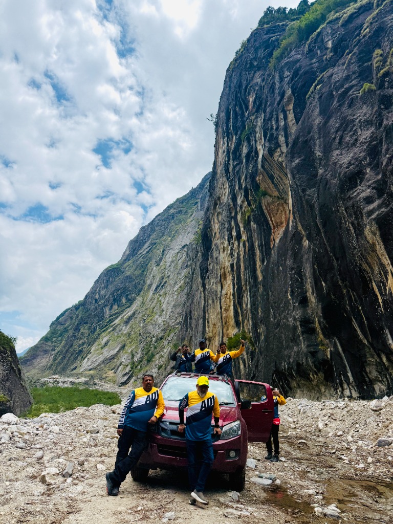 Expedition members and support vehicle under a massive vertical rock wall